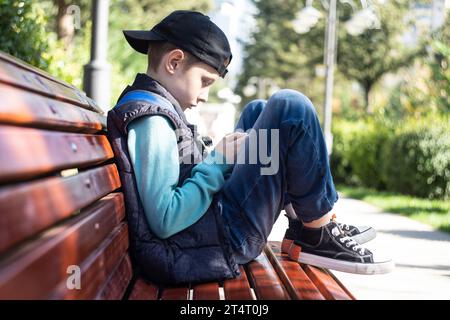 Pre-adolescent boy sitting on a park bench in autumn looking at his mobile phone, Belarus Stock Photo