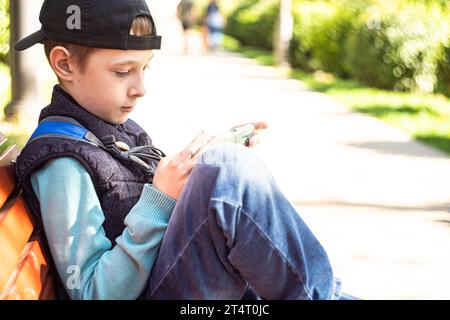 Pre-adolescent boy sitting on a park bench in autumn looking at his mobile phone, Belarus Stock Photo
