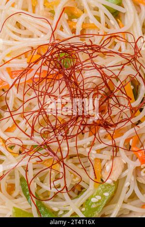 Tasty dish of Asian cuisine with rice noodles, chicken, asparagus, pepper, sesame seeds and soy sauce on dark concrete background Stock Photo