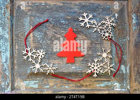 Christmas decoration, New Year's toys: red Christmas tree cut out of cardboard, and wooden snowflakes with red ropes laid out on an old wooden surface Stock Photo