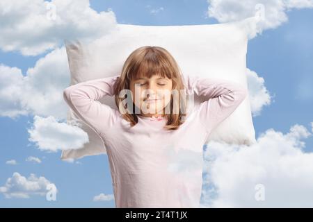 Cute girl in pajamas sleeping on a pillow up in the sky with clouds around Stock Photo