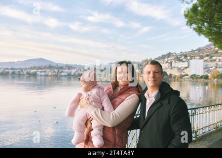 Outdoor portrait of happy young couple with adorable baby girl enjoying nice view of winter lake Geneva or Lac Leman, Montreux, Switzerland Stock Photo