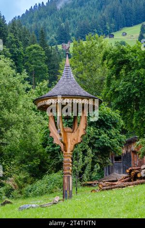 Elaborately carved wooden post with bell, pointed roof & weather vane on top outside a home in the alpine village of Alpbach, Western Austria. Stock Photo