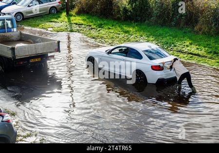 A woman pushes a broken down white BMW car stranded in a flooded road after heavy rainfall and high tide on the River Test estuary in Southampton Stock Photo
