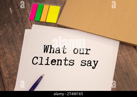 What Our Clients Say statement on paper note pad. Office desk with electronic devices and computer, wood table from above, concept image for blog titl Stock Photo