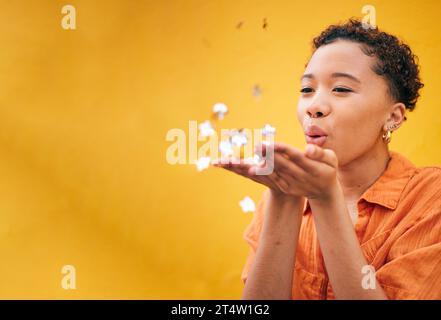 Blowing, petals and African woman on orange background for natural beauty, skincare and romance. Flowers, happy and female person with floral confetti Stock Photo