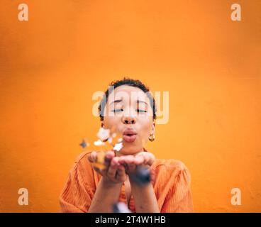 Blowing, petals and face of woman on orange background for natural beauty, skincare and romance. Flowers, happy and female person with floral confetti Stock Photo