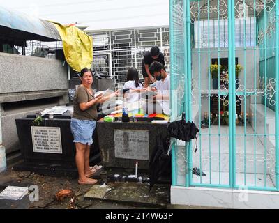 Caloocan, Philippines. 01st Nov, 2023. A family seen eating their packed food on top of the tomb of their departed kin at Sangandaan Cemetery. People flock to Sangandaan Cemetery to observe UNDAS or All Saints Day in Caloocan City despite heavy downpours to visit their departed loved ones. The Philippine National Police (PNP) Caloocan were deployed outside the cemetery ensuring the order and safety of the public. Credit: SOPA Images Limited/Alamy Live News Stock Photo