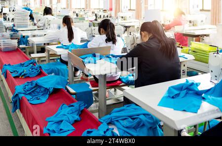 Rear view of chinese female blue collar workers working in clothing factory in a row Stock Photo