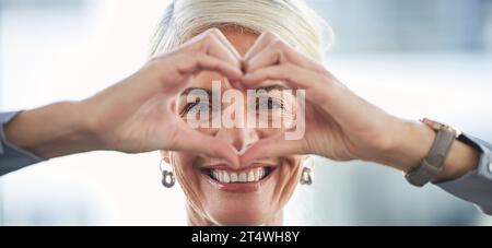 Portrait, hands and heart with a business woman in the office, feeling love for her corporate career. Face, emoji or hand sign with a senior female Stock Photo