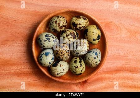 Quail eggs in a wooden bowl on a wooden background, top view Stock Photo