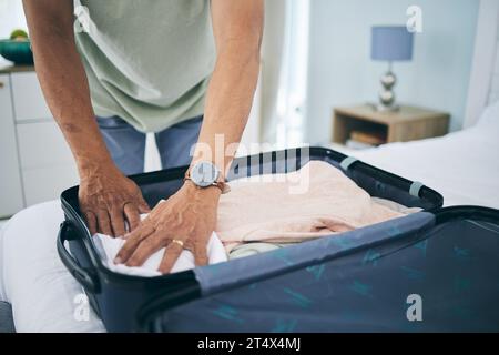Man, hands and packing suitcase in home for travel, holiday trip and vacation. Closeup, person in bedroom and prepare clothes in luggage bag for Stock Photo