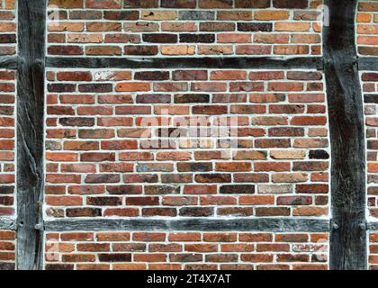 Weathered timber frame wall with bleached wooden beams and red brick stones. Background or texture. Stock Photo