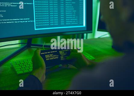 Computer hacker, coding and a man with phone for phishing, scam or cybersecurity software. Online crime, smartphone screen and cyber thief person with Stock Photo