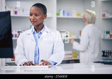 Pharmacist, typing and black woman on computer in pharmacy, drugstore or shop. Wellness, medical professional and African doctor on internet for Stock Photo