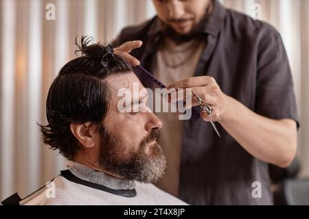 Barber using scissors and comb to cut hair of customer in hair salon Stock Photo