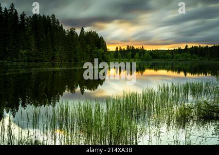 Landscape in the Black Forest. Beautiful lake Windgfällweiher . The sunset sky is reflecting in the water. Long exposure shot with blurred clouds. Ger Stock Photo