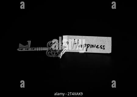 Old decorative key and handwritten tag 'Happiness' tied with straw rope on black background Stock Photo