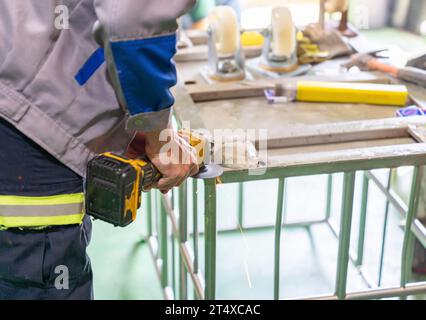 Man polishes cart base wheel with a wireless grinding machine in workshop. Stock Photo