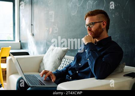 Serious young modern man using laptop sitting on a coworking Stock Photo