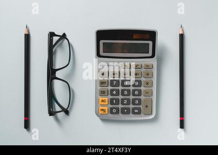 Top view of calculator, glasses, pen and green plant on blue office desk Stock Photo