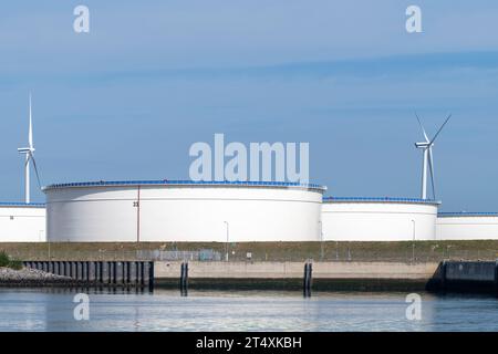 Number of petrochemical storage tanks in a tank farm along the river in the harbor of Rotterdam, the Netherlands with two wind turbines or windmills i Stock Photo