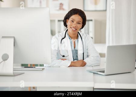 Medical doctor working on laptop and desktop computer, networking with people online and sitting at a desk at a hospital. Portrait of a black female Stock Photo