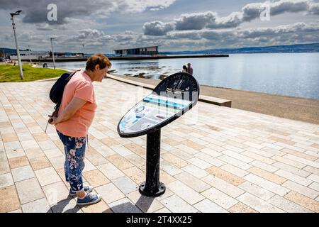 Tourist looking at one of the Clyde Sea Lochs Trail information panel's with the leisure centre and pier in the background at Helensburgh, Scotland Stock Photo