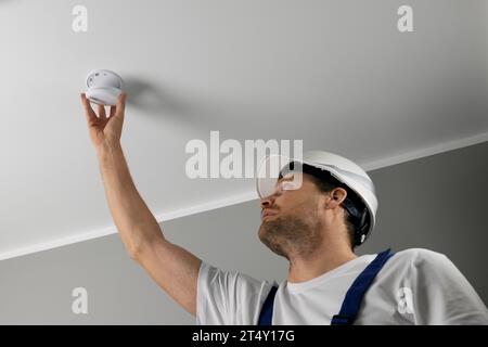 fire safety engineer installing photoelectric smoke detector on house ceiling. home security and fire alarm system Stock Photo