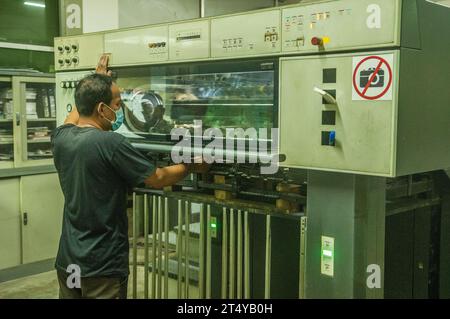 A Cambodian man, wearing a protective face mask, runs a modern printing press. Stueng Mean Chey, Phnom Penh, Cambodia. © Kraig Lieb Stock Photo