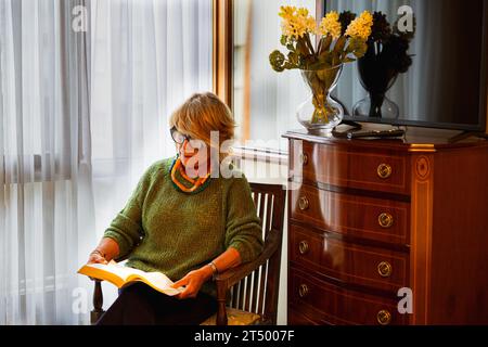 Relaxed older woman sitting in bedroom reading Stock Photo