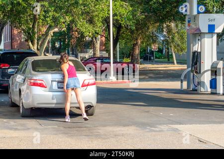 NEW ORLEANS, LA, USA - AUGUST 18, 2023: Young woman cleaning rear car window at a Chevron Station in the Carrollton Neighborhood Stock Photo