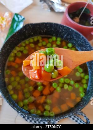 Wooden spoon holding sip of soup consist of carrots and peas Stock Photo