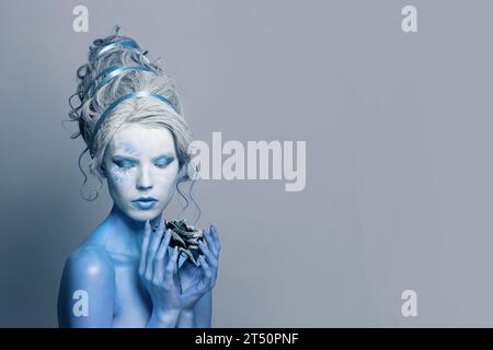 Beautiful model woman with blue skin, stage makeup and hairstyle with black rose flower on gray background Stock Photo