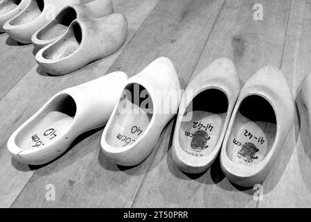 A line of traditional Dutch wooden clogs arranged on the floor, in grayscale Stock Photo