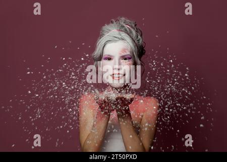 Beautiful woman with stage makeup and white snow on colorful pink background. Winter party, Halloween  carnival and theater concept Stock Photo