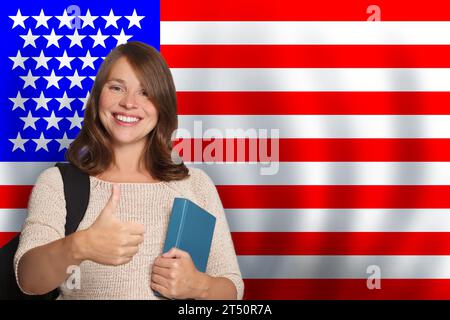 Happy woman student showing thumb up against US flag background. Travel, education and learn language in USA concept Stock Photo