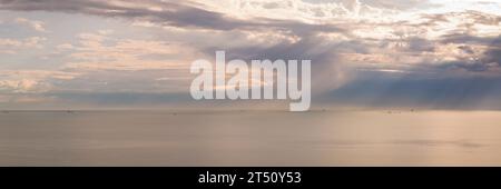 Panorama of stormy sky with sun rays piercing the clouds, flat sea at dawn, minimalist photo and mystery mood. Stock Photo