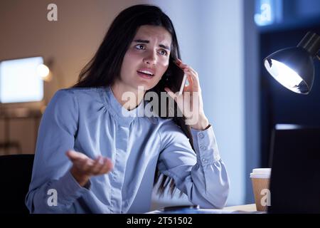 Phone call, question and angry business woman talking, chatting or speaking to contact in office at night. Technology, questions and upset or confused Stock Photo