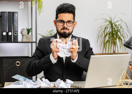 Angry furious Arab man working at office throwing crumpled paper, having nervous breakdown at work, migraine headache, stress management, mental distress problems, losing temper, reaction on failure Stock Photo