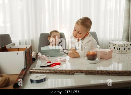 Cute boy and girl are sitting at the table. Packing a gift. Stock Photo