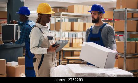 Diverse team of employees scanning boxes barcodes, looking at merchandise in cardboard packages. Two people bringing products to supervisor, using digital tablet to scan goods. Stock Photo