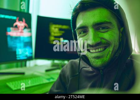 Cybersecurity, crime and smile, portrait of hacker in neon office with code, fraud and virus. Software, ransomware and face of happy man on cyber Stock Photo