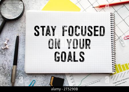 Inspirational quote - Stay focused on your goals. With text message on white paper book, pen, a cup of morning coffee, flower. Stock Photo