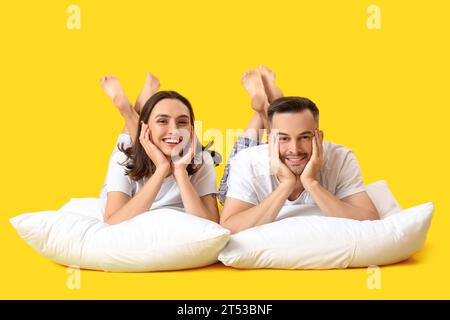 Young couple with pillows lying on yellow background Stock Photo