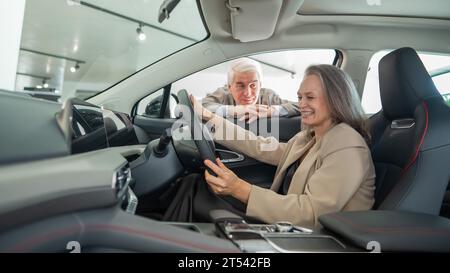 An elderly couple chooses a new car at a car dealership. Mature woman driving.  Stock Photo