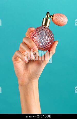 Anonymous female with manicured fingers demonstrating while holding crystal perfume glass bottle with pink bulb spray mounting in hand against blue ba Stock Photo