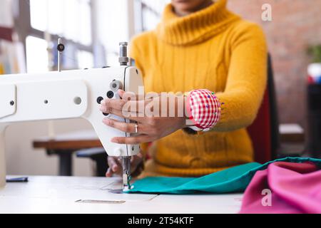 Biracial female fashion designer using sewing machine in sunny studio Stock Photo