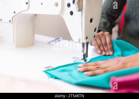 Biracial female fashion designer using sewing machine in sunny studio Stock Photo