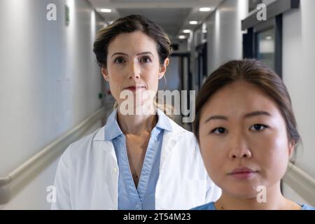 Two diverse female doctors standing single file in hospital corridor Stock Photo